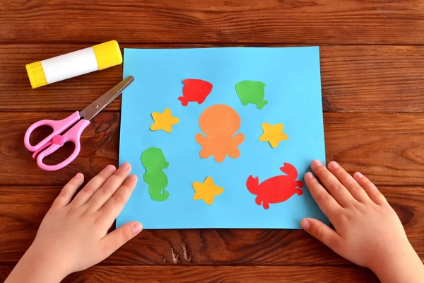 Карта з морськими тваринами і рибою. Дитячі ремесла ідея проекту. Клей, ножиці. Дитина поклала руки на стіл — стокове фото