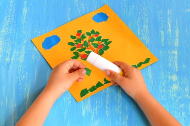 Çocuk yırtık bir kağıt ağacı yapar. Çocuk elinde yeşil bir kağıt parçası tutar ve yapışır. Yaz ağacı kağıt zanaat. Okul öncesi çocuklar için fikir.