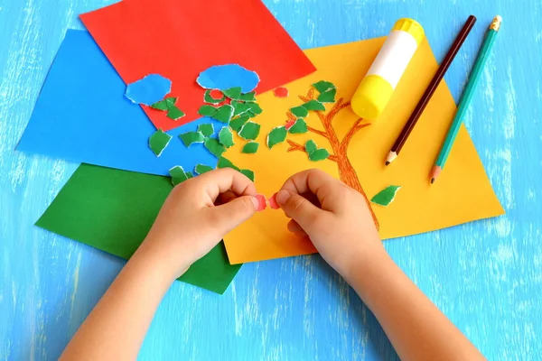 Barn tårar ett rött papper i små bitar. Barn håller röda pappersbitar i händerna. Uppsättning av färg papper, blyertspennor, lim pinne på trä bakgrund. — Stockfoto