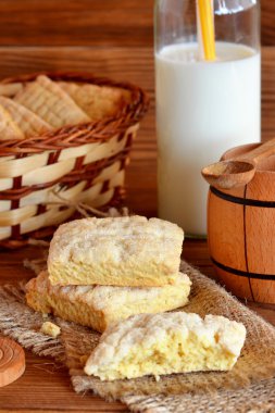 Bir çuval lezzetli ev kurabiyeleri. Sepette bir demet bisküvi. Cam şişede sütü. Küçük dekoratif varil ve kaşık. Tahta masa. Rustik tarz. Dikey fotoğraf. Closeup