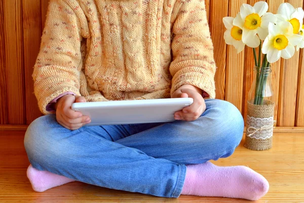El niño se sienta sosteniendo una tableta en las manos. Jarrón de narcisos. Fondo de madera — Foto de Stock