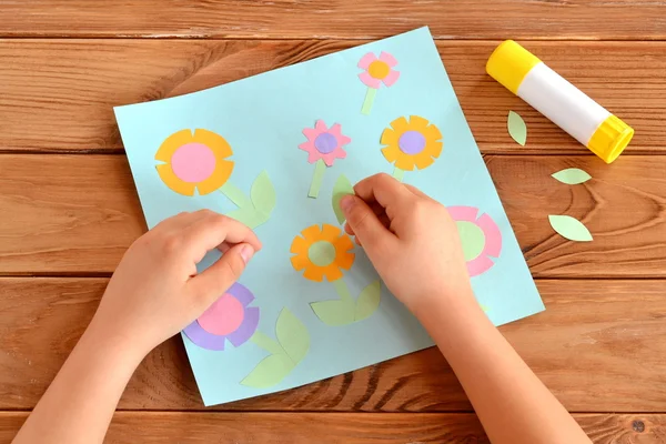 Dziecko robi karty z kwiatami. Dziecko w ręce trzyma liść papier i wbija go. Klej, nożyczki, z życzeniami na drewnianym stole. Ręczniki papierowe kwiat dla dzieci. Projekt artystyczny dla dzieci. — Zdjęcie stockowe