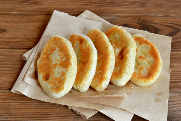 Filled fried pies on paper and brown wood background. Deliciously simple recipe — Stock Photo, Image