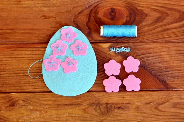 Felt Easter egg with flowers on a brown wooden background. Sew the flowers to the felt egg. Sewing set — Stock Photo, Image