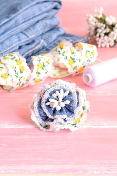 Hermoso broche de flores de vaqueros viejos. Reciclar accesorios vaqueros. Jeans, encaje, hilo, aguja sobre fondo de madera rosa. Foto vertical — Foto de Stock