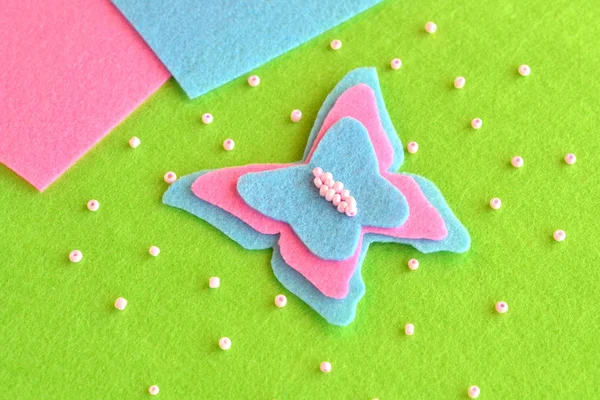 Felt butterfly on a green background, beads, blue and pink sheets. Easy children's crafts. Butterfly sewing for kids. DIY easy sewing for kids projects — Stock Photo, Image