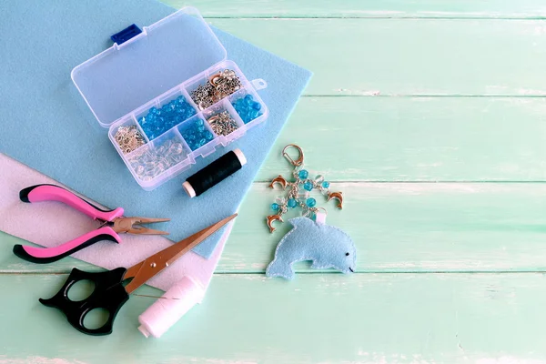 Söta filt Dolphin nyckelring med pärlor. Blå filt havet djur nyckelring. Material och verktyg till att skapa hantverk. Sommar barn kreativitet. Barn arbetsplatsen. Blå trä bakgrund med tomt utrymme för text — Stockfoto