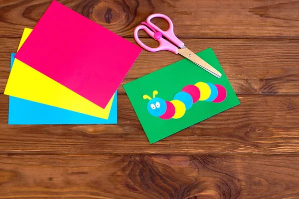 Apliques de papel para niños oruga de color en la hoja verde, hoja de papel, tijeras. Fondo de madera marrón — Foto de Stock