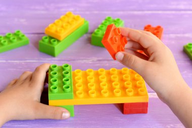 Alt yapı taşları oyuncaklar elinde tutar ve yatak yapar. Lila ahşap arka plan üzerinde çocuklar için yapı taşları oyuncaklar. Kids hareket anaokulu ya da evde 