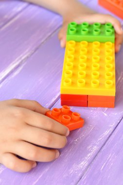 Alt yapı taşları oyuncaklar elinde tutar ve çalış. İnce motor becerilerini geliştirmek yapı taşları seti çocuklar. Anaokulu öğrenme oyun ve etkinlik. Lila ahşap arka plan. Portre 