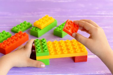 Küçük çocuk bir tasarımcı elinde engeller ve oyuncak yatak barındırır. Lila arka plan üzerinde renkli plastik Oluşturucu. Oyuncak yapı taşları oyunu. Çocuk masters ince motor becerileri 