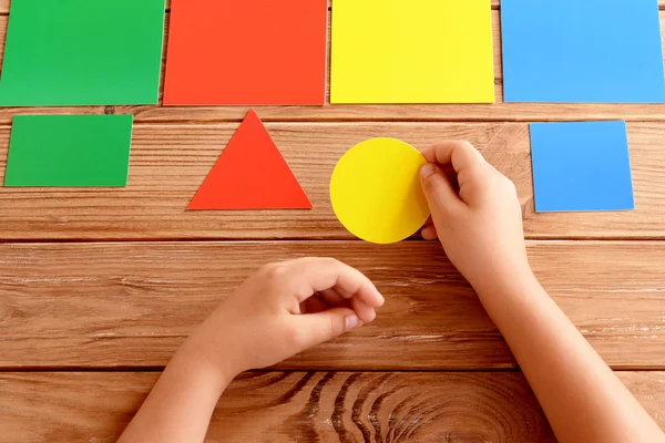El niño sostiene un círculo de cartón amarillo en sus manos y se pone una tarjeta de color correspondiente. El niño aprende colores. Conjunto de tarjetas de colores para niños en edad preescolar. Idea para aprender en el jardín de infantes, en casa — Foto de Stock