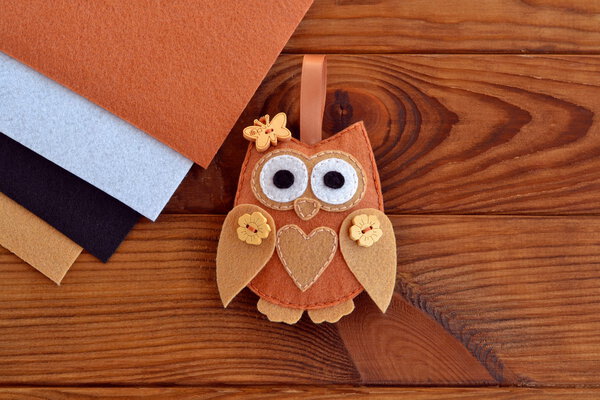 Home decor cute toy on wooden background. Felt owl sewing pattern. Soft owl embellishment or ornament. Brown, white, beige and black felt sheets