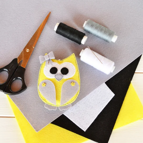 Cute felt owl toy decorated with bow and buttons. Stuffed animal owl on wooden background. Home decor plush toy. Felt sheets, scissors, thread, needle, pins. Top view — Stock Photo, Image