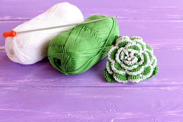 Inicio hecho verde y blanco flor de ganchillo decorado con perlas. Dos madejas de hilo de algodón y ganchillo gancho sobre fondo de madera lila — Foto de Stock