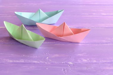 Leylak ahşap masa üzerinde üç renkli origami gemisi. Origami tekneleri yapmak kolay. Çocuklar için DIY origami tekneleri. Yaz gazetesi çocuklar için aktivite fikri üretiyor. Katlanan kağıt işçiliği.