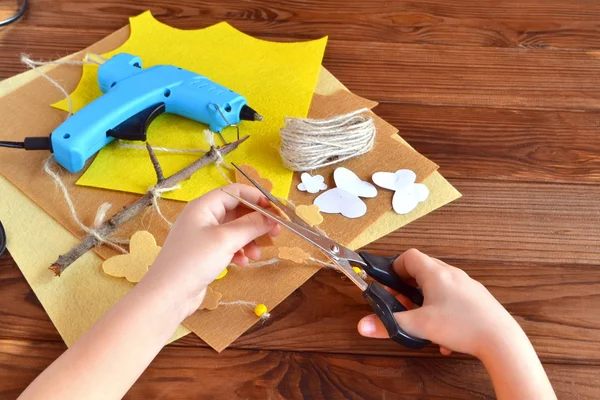 Kind houdt de schaar en de vilten bloem uitgesneden. Schaar, hete lijmpistool, bladen van vilt, decoratieve hanger met vilten vlinders en bloemen — Stockfoto