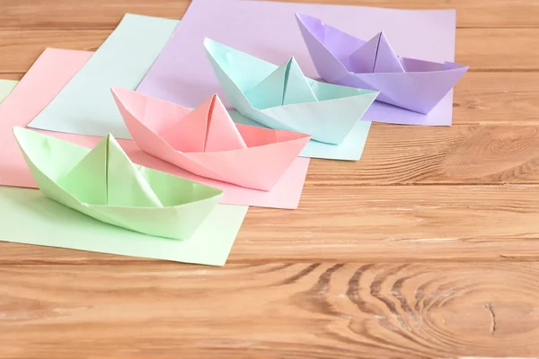 Four colored origami boats toys on a wooden table. Square sheets of colored paper. Creative paper crafts idea for summer vacation