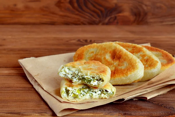 Kızarmış pies ev yapımı peynir, yeşil soğan ve dereotu kağıt ve tahta arka plan ile. Maya-Alerjik börek tarifi. Rustik bir stil. Portre — Stok fotoğraf