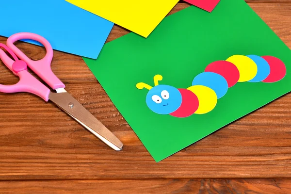 Детская бумага аппликация - цветная гусеница на зеленом листе, лист бумаги, ножницы. Коричневый фон — стоковое фото