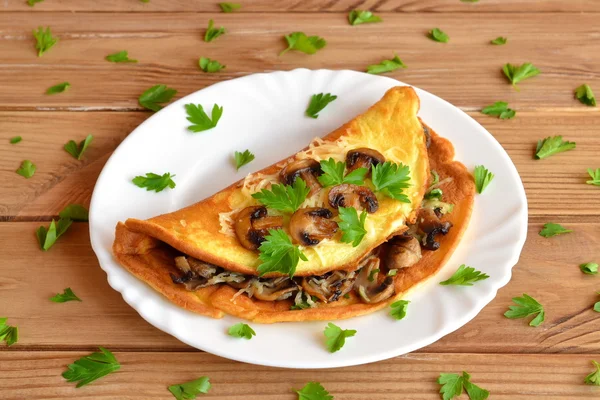 A tasty omelet with mushrooms, cheese and parsley. Stuffed omelet on a plate and on a wooden table. Eggs recipe. Quick vegetarian breakfast idea — Stock Photo, Image