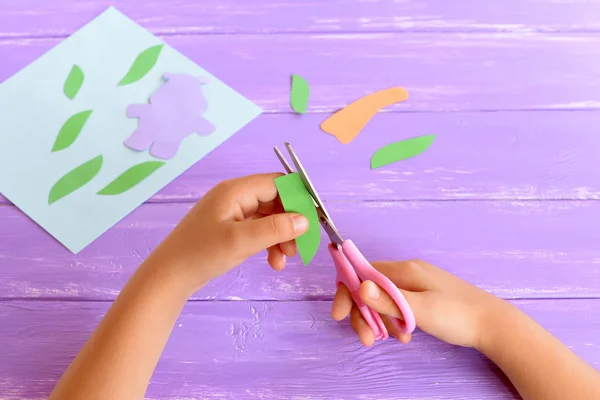 Barn klipper ett blad från grönboken. Ungen har sax i händerna. För att skapa ett kort. Barn gör hantverk från färgat papper. Konstprojekt för dagis, sommarläger — Stockfoto