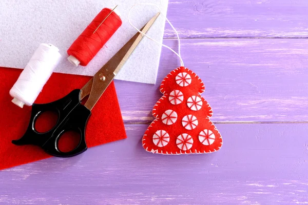 Red felt Christmas tree ornament, scissors, red and white felt sheets, thread, needle lilac on wooden background with blank space for text. Home decor Christmas tree hand made. Crafts idea for Christmas. Handwork diy craft ideas — Stock Photo, Image