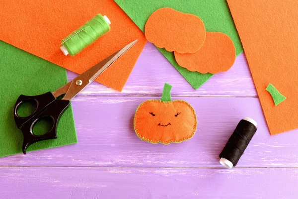 Easy sew stuffed fabric pumpkin decoration, threads, scissors, needle, felt sheets and patterns on lilac wooden table. Halloween pumpkin idea made with felt. Kids Halloween background — Stock Photo, Image