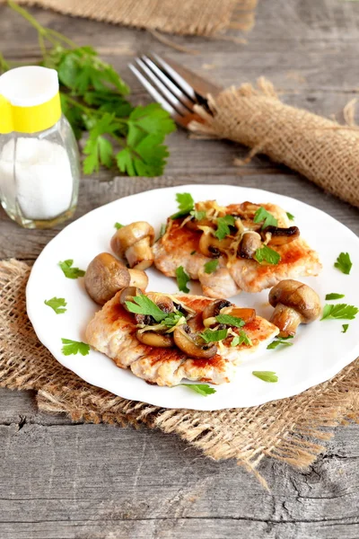 Filetes de pavo frito con queso, champiñones y perejil en un plato y en una arpillera. Perejil verde fresco, salero, tenedor en una mesa de madera. Cómo cocinar la carne. Cocinar pechuga de pavo. Primer plano. — Foto de Stock