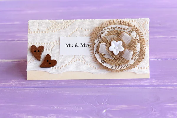 Vintage wedding invitation on lilac wooden background. Homemade wedding invitation card made of paper, lace, burlap, wooden buttons, plastic flower. Elegant card crafts — Stock Photo, Image