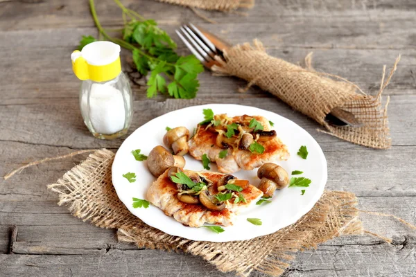 Steak payudara Turki panggang dengan keju dan jamur di atas piring. Garam shaker, garpu, pisau, peterseli mentah segar di meja pedesaan tua. Memasak daging kalkun — Stok Foto