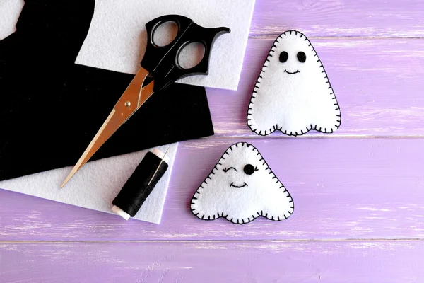 Two small white ghosts crafts, felt sheets, scissors, thread, needle on lilac wooden background. Hand Halloween decor idea for kids. Halloween sewing craft — Stock Photo, Image