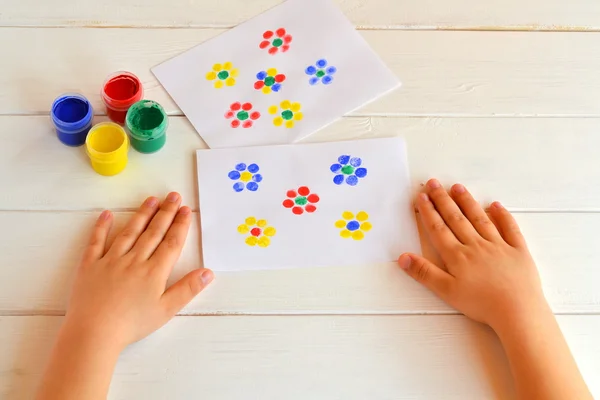 İki resmi çiçek çocuk parmak boyalı. Kavanoz guaş ile. Çocuk ellerin masada — Stok fotoğraf