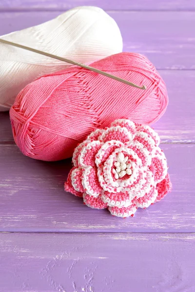 Zuhause rosa und weiß gehäkelte Rose zwei Knäuel Baumwollgarn und Häkelnadel auf fliederfarbenem Holzhintergrund. niedlichen Perlen Blumenmuster Foto. Hand schöne Blume Idee — Stockfoto