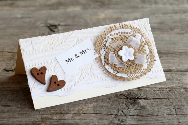 Vintage wedding invitation on old wooden table. Handmade wedding invitation card decorated with lace and burlap flower and wooden hearts. Lovely card crafts. Closeup — Stock Photo, Image