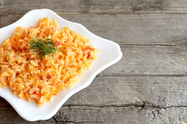 Sebzeli risotto bir tabakta servis edilir. Pirinç domates, havuç, sarımsak ve baharat ile pişirilir. Metin için boş alana sahip eski ahşap arka plan. Closeup 