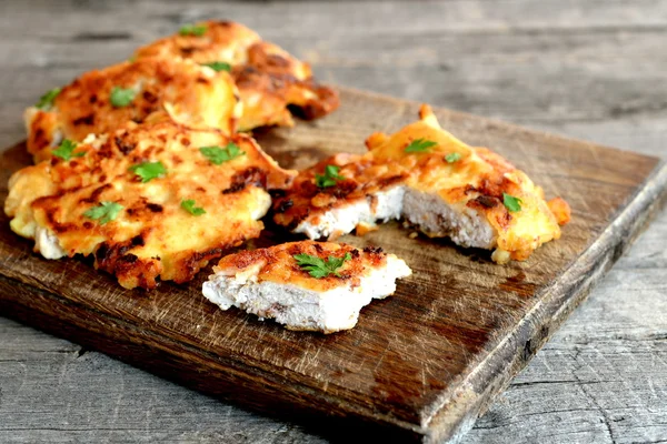 Pedaços de carne de peru fritos em massa e decorados com folhas de salsa. Corte costeletas assadas de peru em uma tábua de corte e um velho fundo de madeira. Cozinhar aves de capoeira — Fotografia de Stock