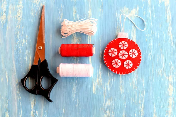 Pelota bordada de fieltro rojo, tijeras, hilo, cordón sobre fondo de madera azul. Bolas de Navidad colgando adornos de costura Tutorial de bricolaje para niños paso a paso. Vista superior. Artesanía para diciembre bricolaje Navidad para niños en casa foto — Foto de Stock