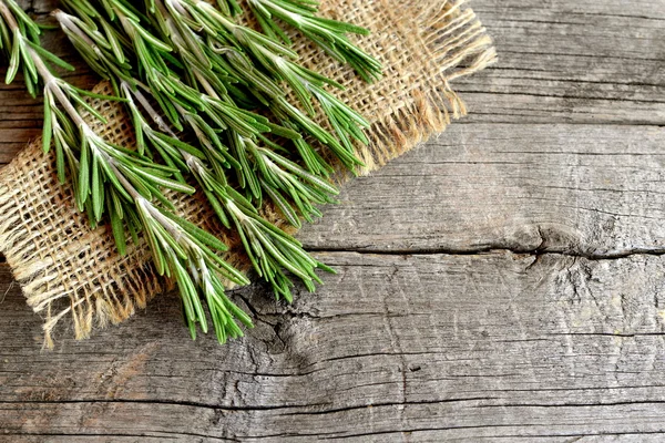 Zelené větvičky čerstvého rozmarýnu na pytlovina a staré dřevěné pozadí s prázdné místo textu. Aromatické rostliny používané v kuchyni, medicína, kosmetika — Stock fotografie