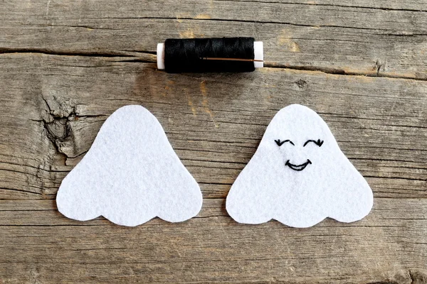 Cut from white felt details for making Halloween ghost decor, thread, needle on a wooden table. On one side embroidered with black thread eyes and mouth. A step instruction for kids. Wooden background — Stock Photo, Image