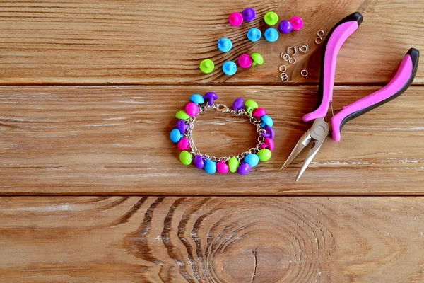 Pulsera botón. Conjunto de botones de colores brillantes, alicates. DIY brazalete idea de joyería. Fácil hacer manualidades creativas. Pulsera hecha de materiales fácilmente disponibles. Fondo de madera con espacio para texto — Foto de Stock