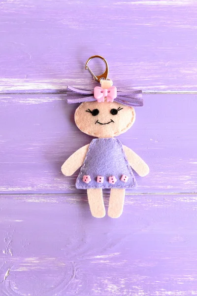 Cute little doll isolated on purple wooden background. Charm keychain for a children bag or backpack. Kids sewing crafts idea — Stock Photo, Image