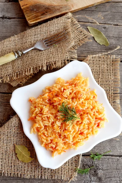Gemüserisotto auf einem Teller, Gabel, Schneidebrett auf altem Holzgrund. Reis mit Tomaten, Karotten, Knoblauch und Gewürzen gekocht. einfaches vegetarisches Reisrezept — Stockfoto