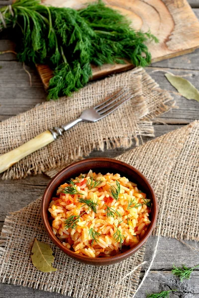 Risotto mit Gemüse in einer Tonschüssel, Gabel, Dillzweigen, Schneidebrett auf altem Holzgrund. Reis mit Tomaten, Karotten, Knoblauch und Gewürzen gekocht. einfache und gesunde vegetarische Reisspeise — Stockfoto