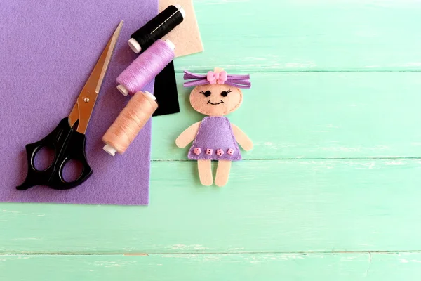 Muñeca linda hecha a mano, tijeras, hilo, aguja, hojas de fieltro sobre fondo de madera con espacio en blanco para el texto. Cómo de simple y barato hacer un juguete para niños. Artesanía creativa de muñecas con fieltro para niños —  Fotos de Stock