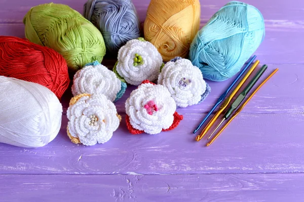 Набор цветов вязания, хлопчатобумажные пряжи, крючки разного размера на фиолетовом деревянном фоне. Красочные вязаные розы. Ремесленная идея для детей и начинающих — стоковое фото
