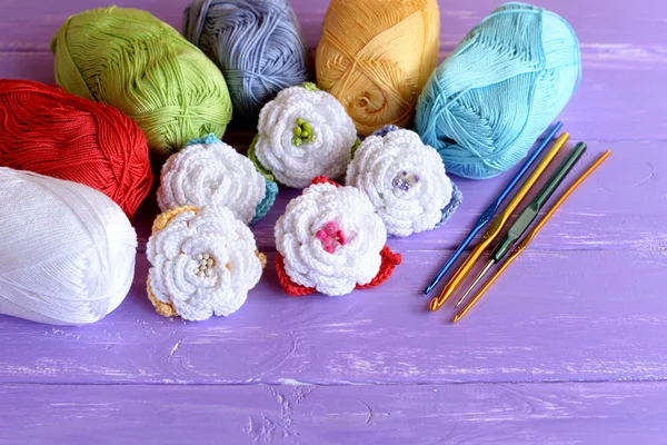 Häkelblumen-Set, Baumwollgarnknöpfe, Haken unterschiedlicher Größe auf lila Holzgrund. bunte gehäkelte Rosen. Bastelidee für Kinder oder Anfänger — Stockfoto