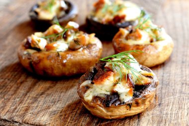 Mantar kapaklar peynir ve et ile doldurulmuş, fırında pişmiş ve ince dal dereotu ile süslenmiş. Ahşap tahta üzerinde mantar meze. Portre