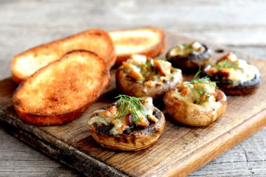 Lezzetli mantar kapaklar peynir ve et ile doldurulmuş ve fırında pişmiş. Beyaz ekmek, kızarmış tost. Ahşap arka plan 