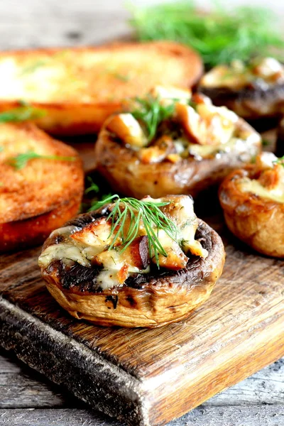 Champiñones rellenos y tostadas fritas en una tabla de cortar y mesa de madera. Gorras de champiñones al horno rellenas con queso y receta de carne. Primer plano. — Foto de Stock